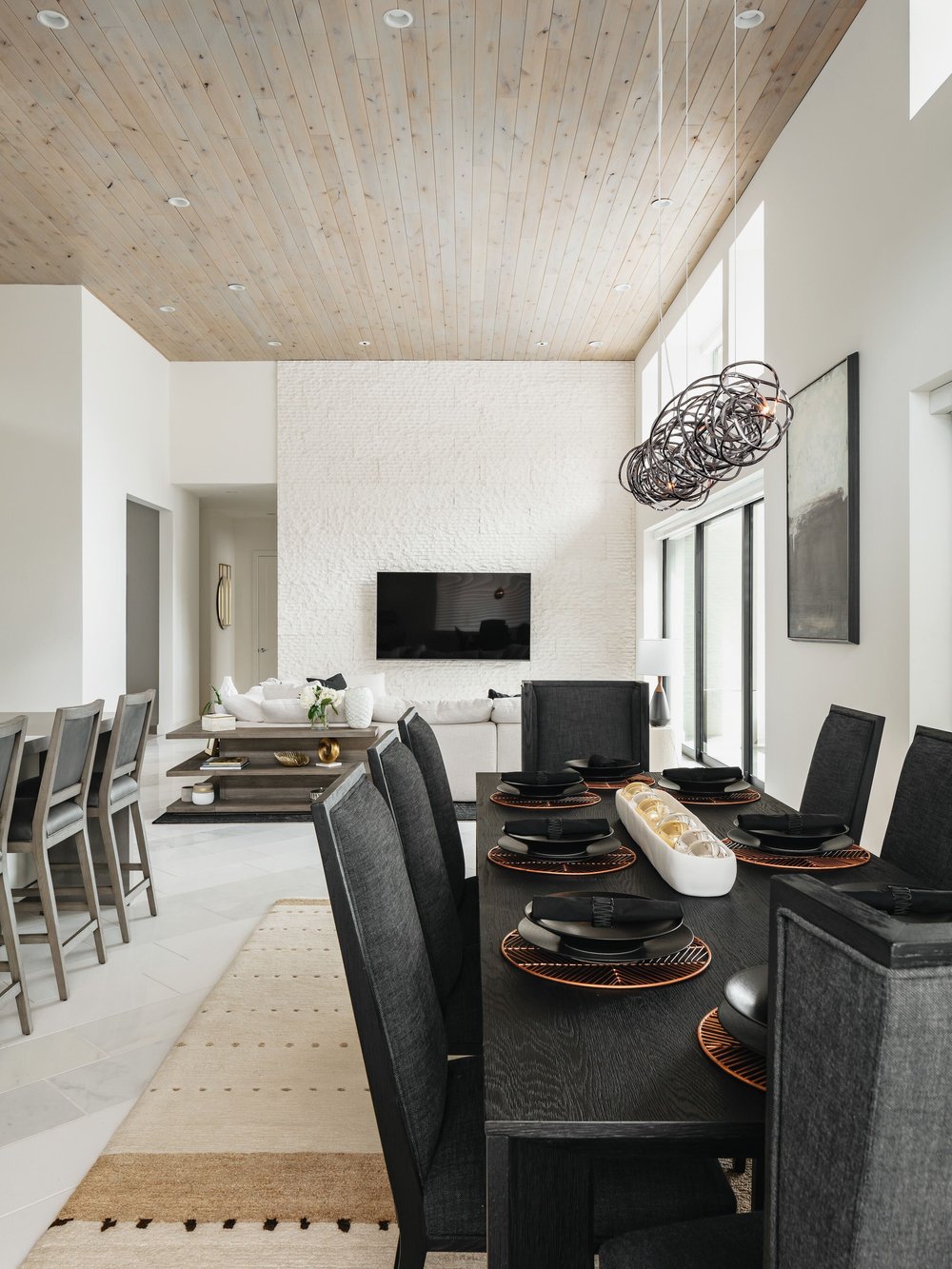 Natural wood textured ceilings in a modern dining room with long, black dining table, black dining chairs with backs.  