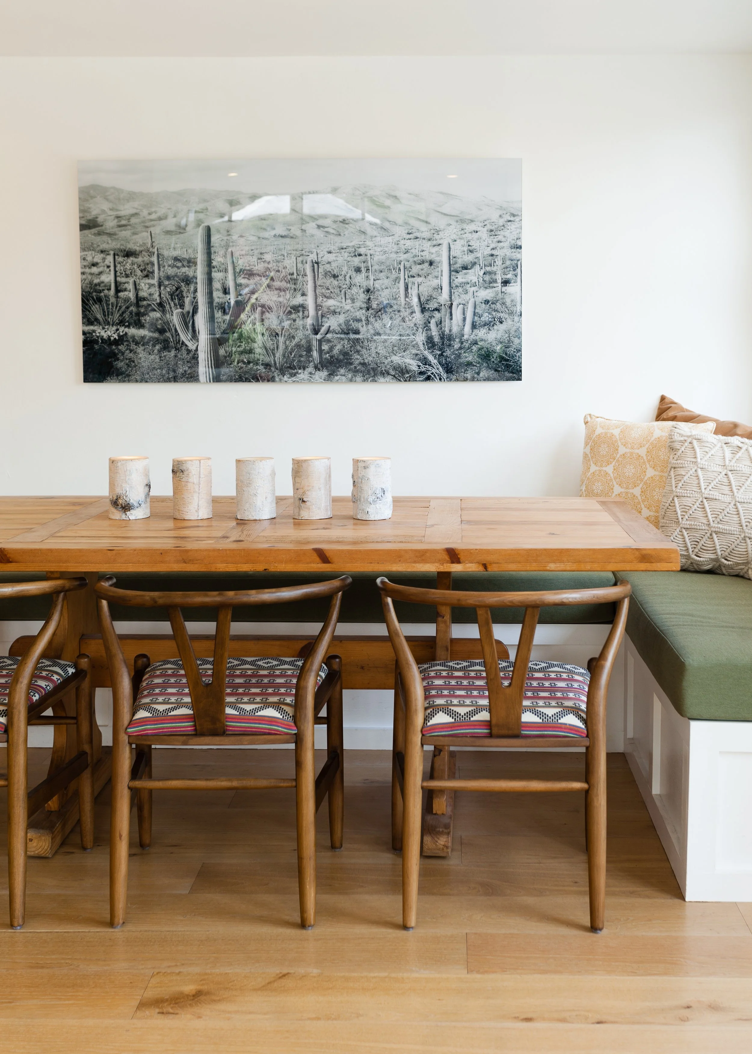 a wooden dining table sitting under a painting on a wall.