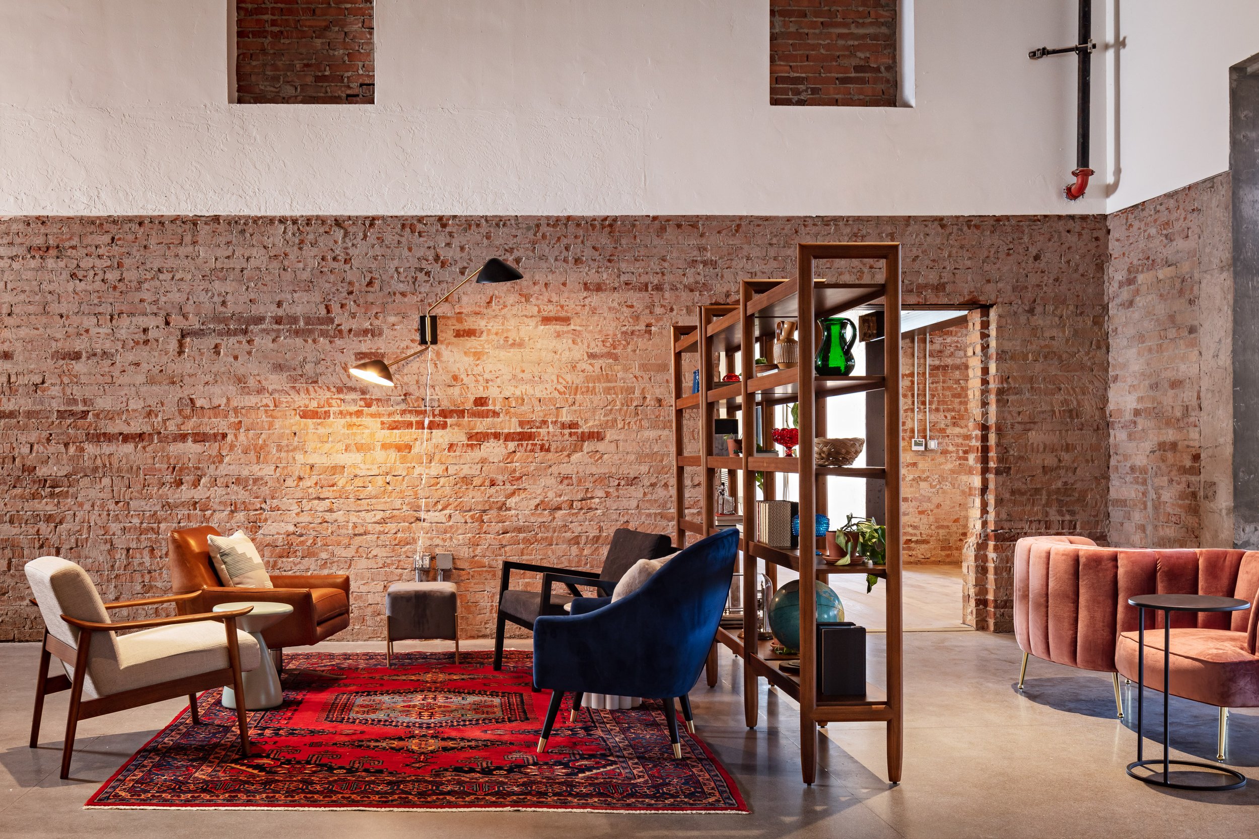 Resimercial design for a Scottsdale office space includes a walnut bookshelf as a room divider, creating a lounge space with mid century modern accent chairs and vintage rug.