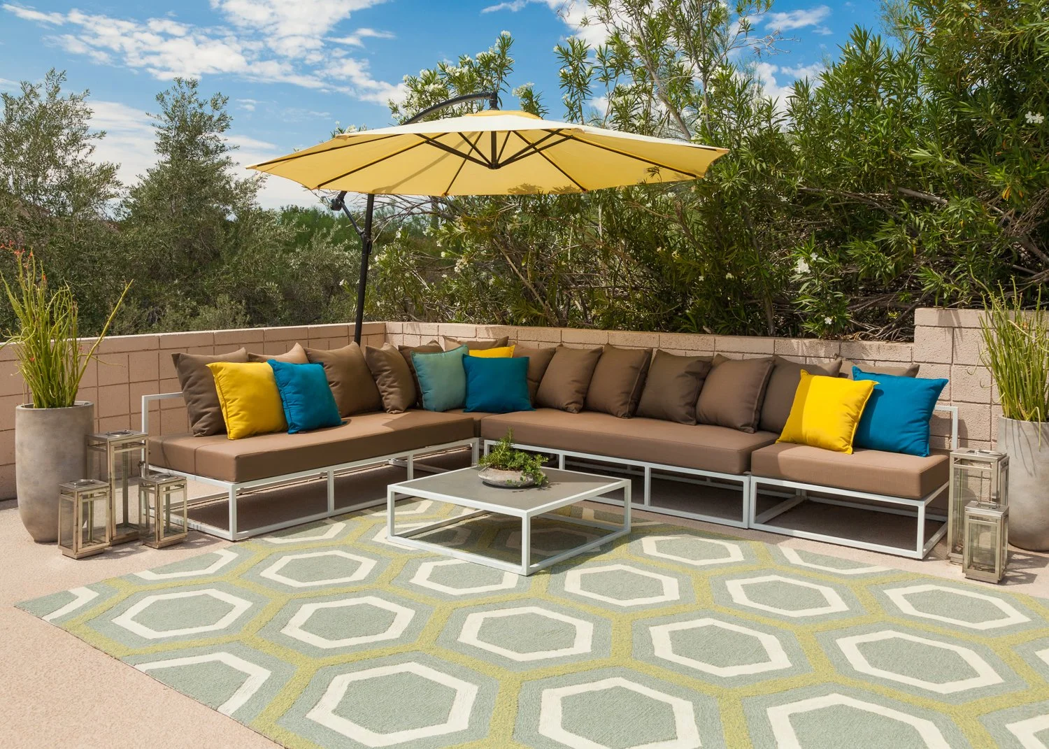 Outdoor sectional sofa with accent pillows, large patio umbrella, square coffee table and geometric patterned outdoor rug.
