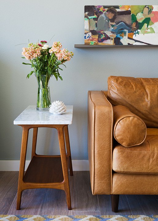 Vintage leather couch, a mid century modern side table, and colorful wall art. Small side table styled with fresh cut flowers.