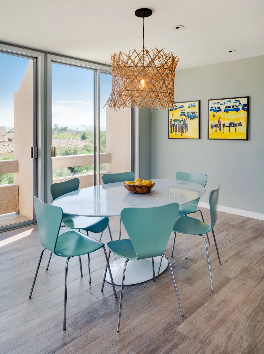 Mid-century modern dining area in a Paradise Valley home with blue chairs, a round white table and sculptural woven pendant light.