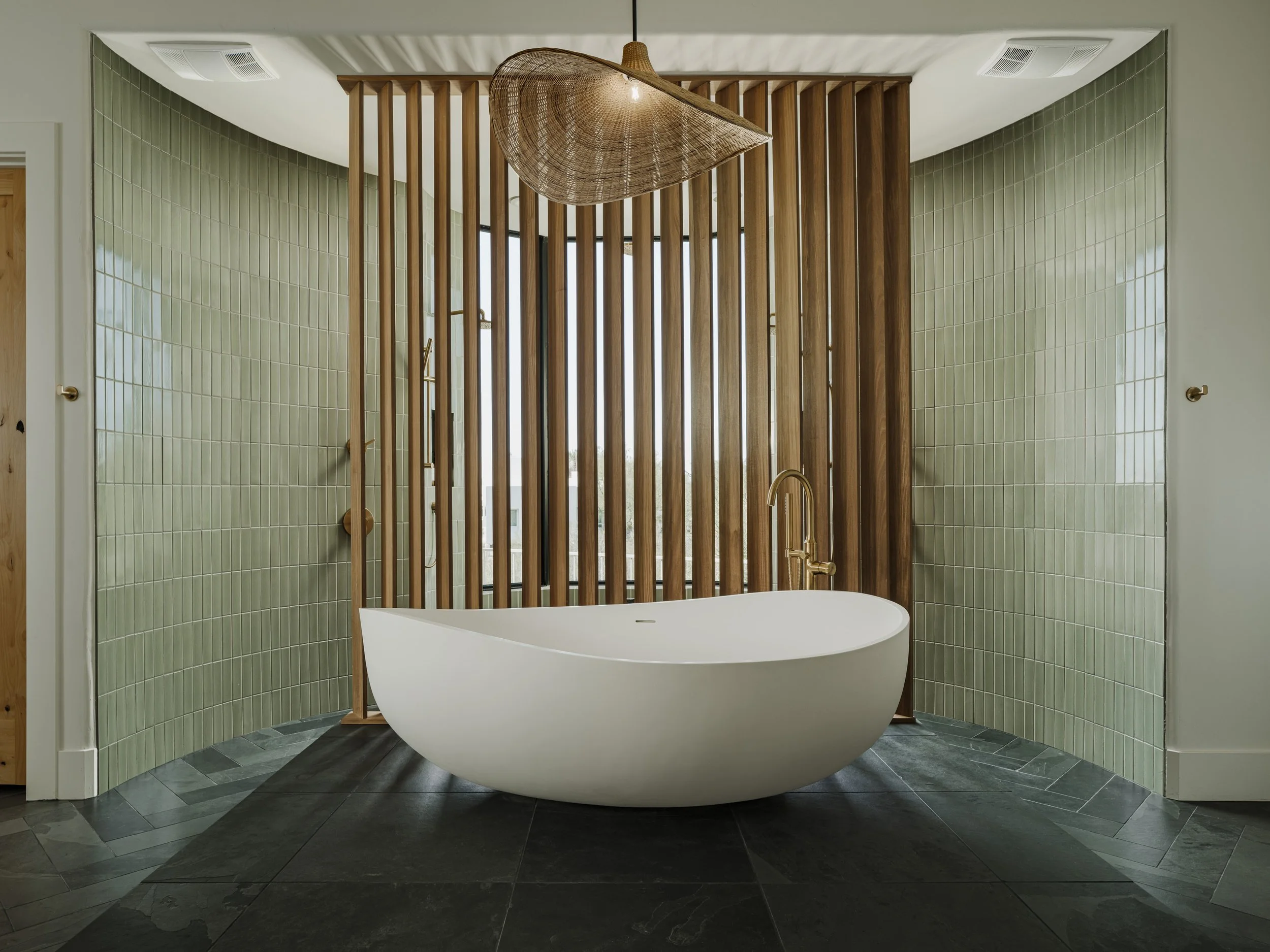 Carefree, Arizona Modern bathroom with a white freestanding bathtub, light green tiled walls, a wooden slatted partition, and a woven pendant light