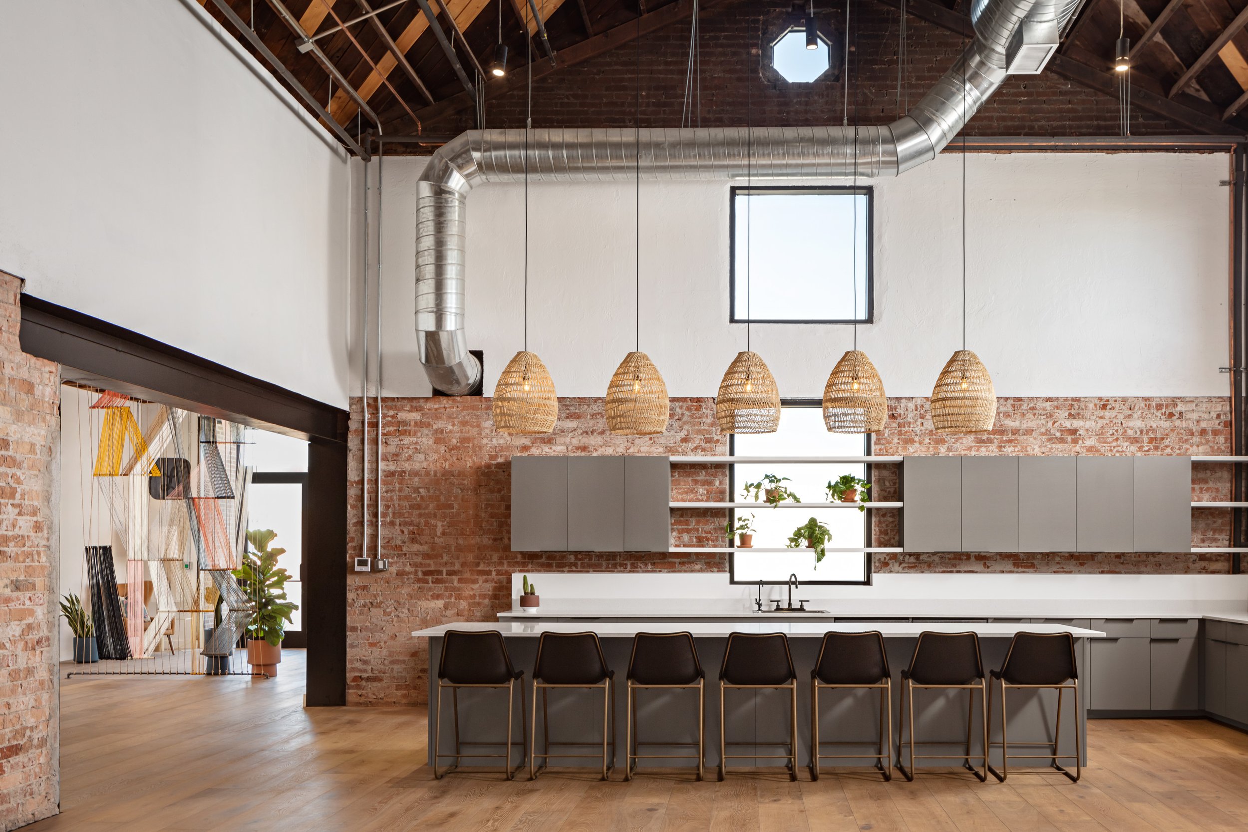 Pendant lights hang from exposed ceilings in the office kitchen at Lemonade Insurance where bar stools with backs line an extra long kitchen island.