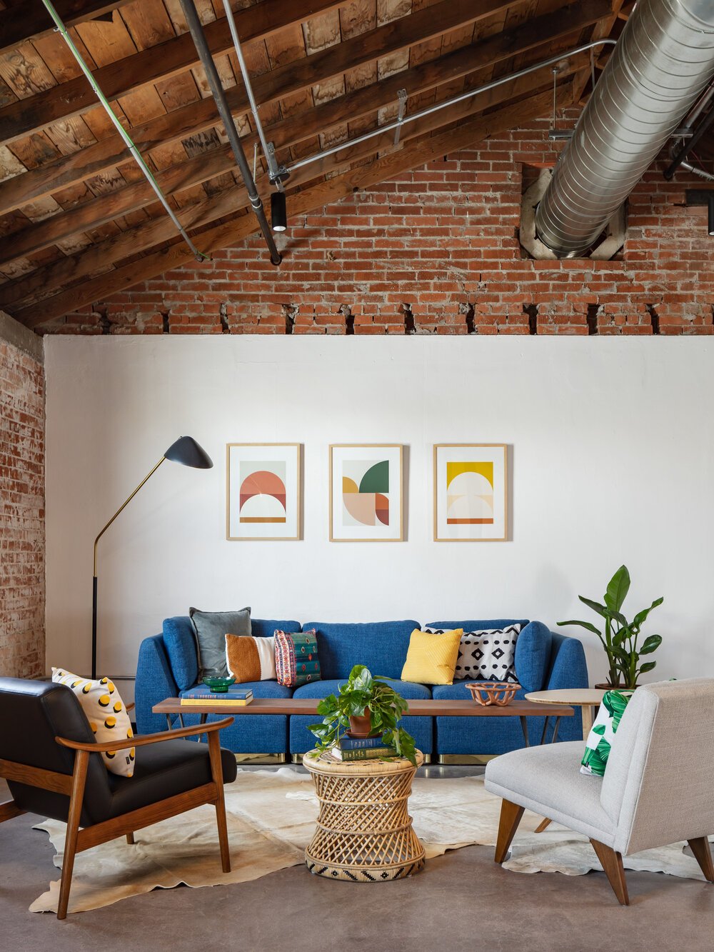Bright blue sofa and mid century accent chairs in a Scottsdale office space with vaulted ceilings and exposed brick wall.