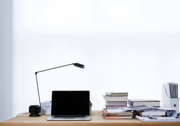 A laptop open on an organized desk space, with books and a lamp.
