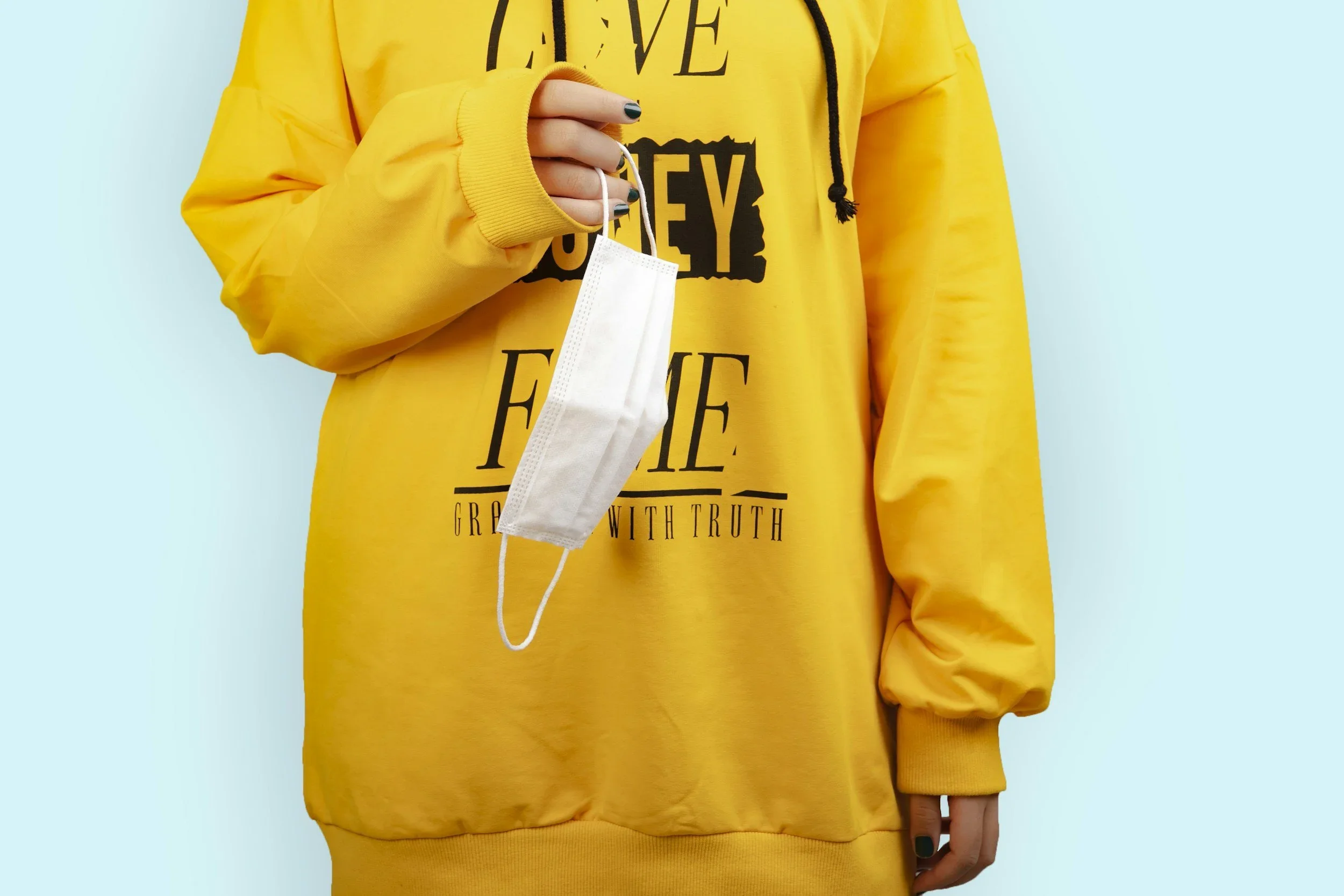 Yellow hoodie holding face mask