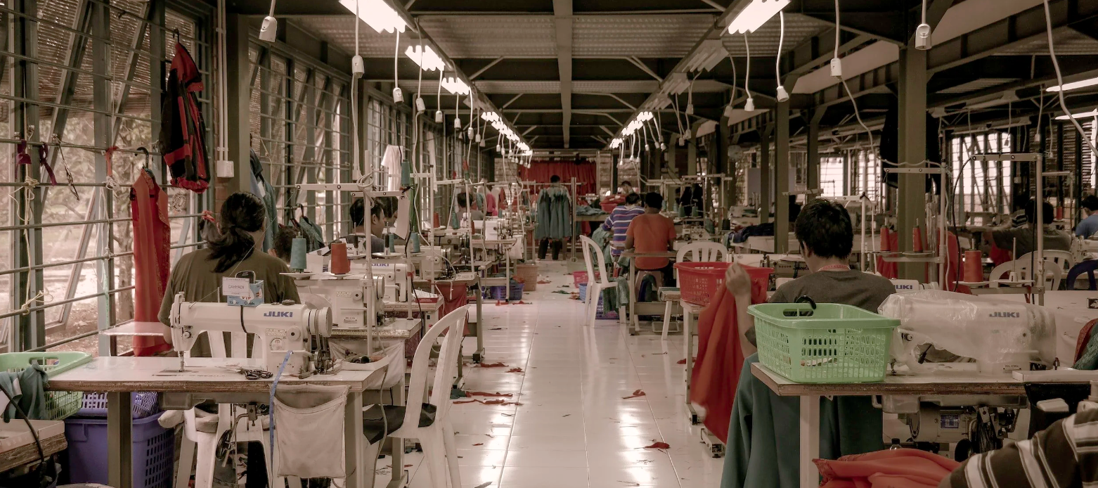 An image of a clothing factory with sewing machines and florescent lights