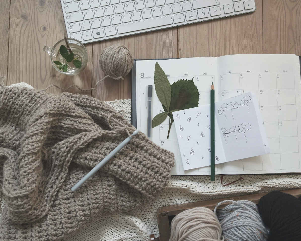 image of someone's desk, with a cup, a yarn project, and a notepad on the desk