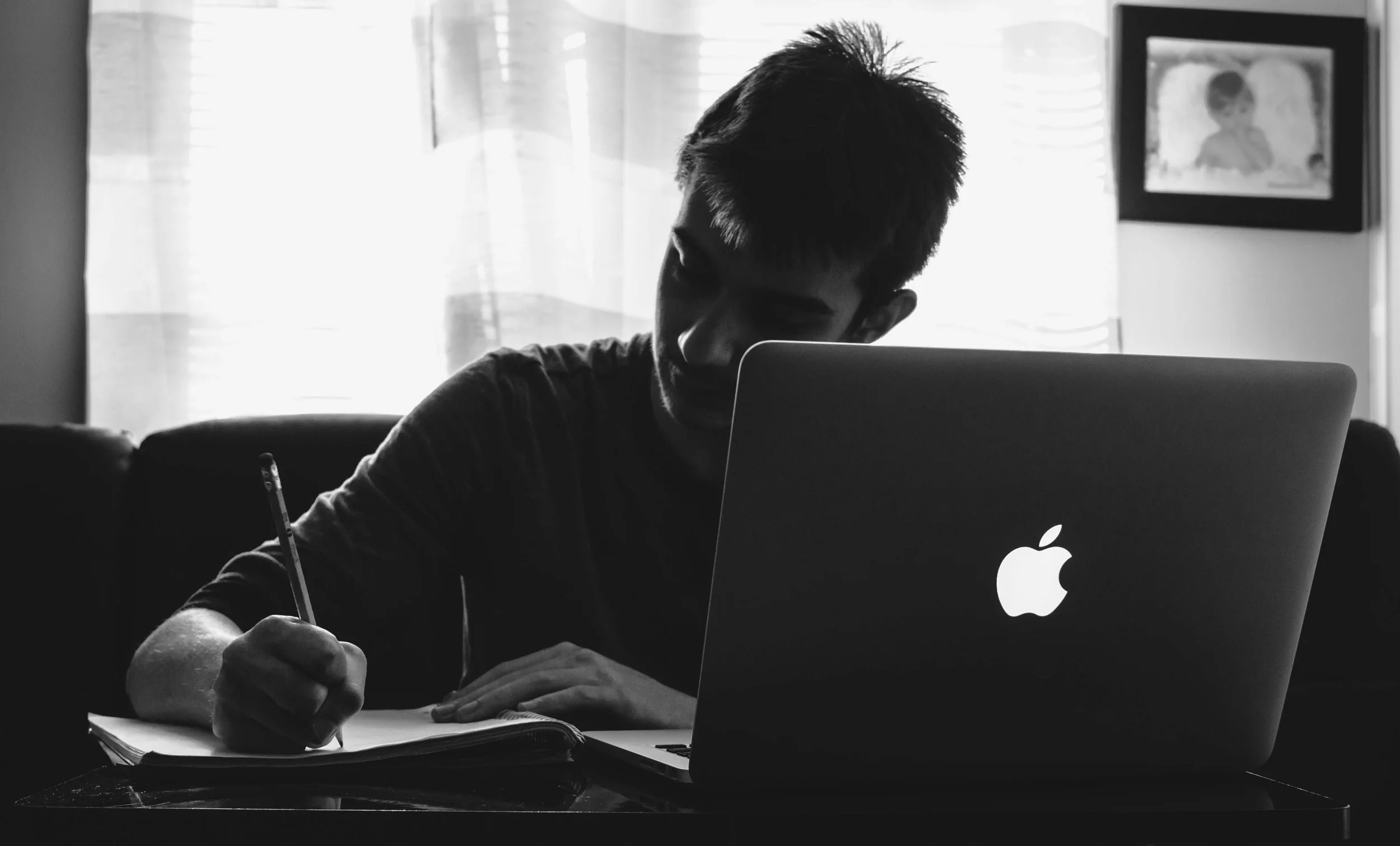 boy writing on a notebook in front of the computer