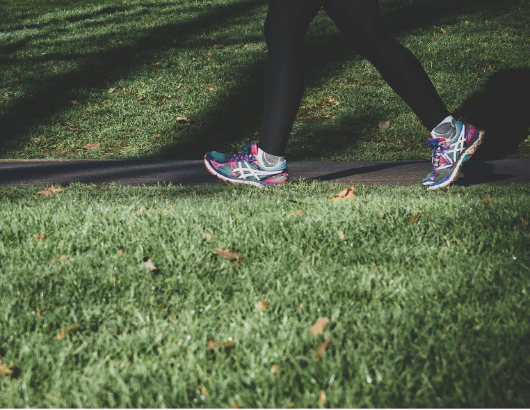 The bottom half of a woman walking through a park.