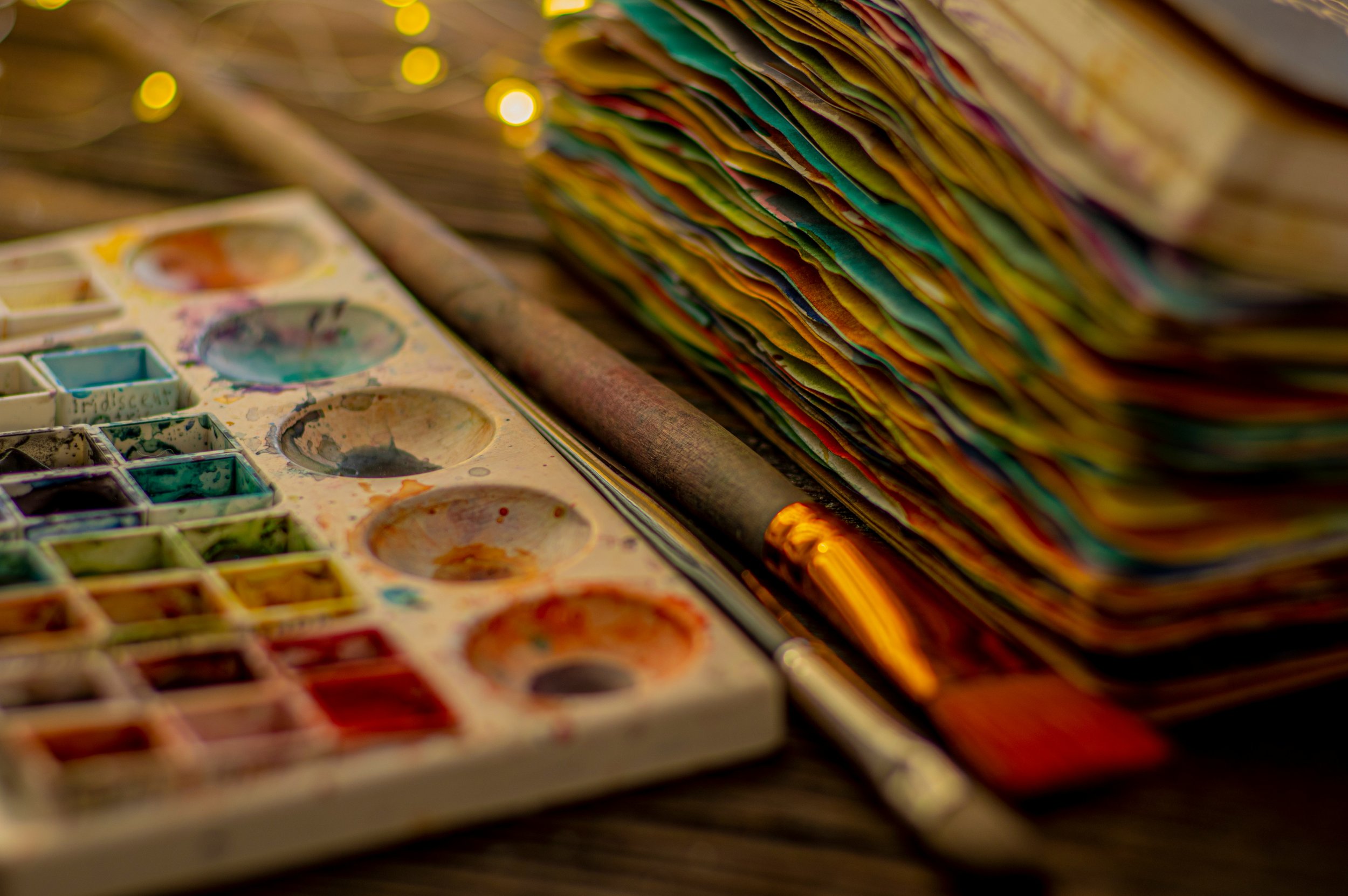 a pile of painted pages, a paintbrush, and a watercolor palette