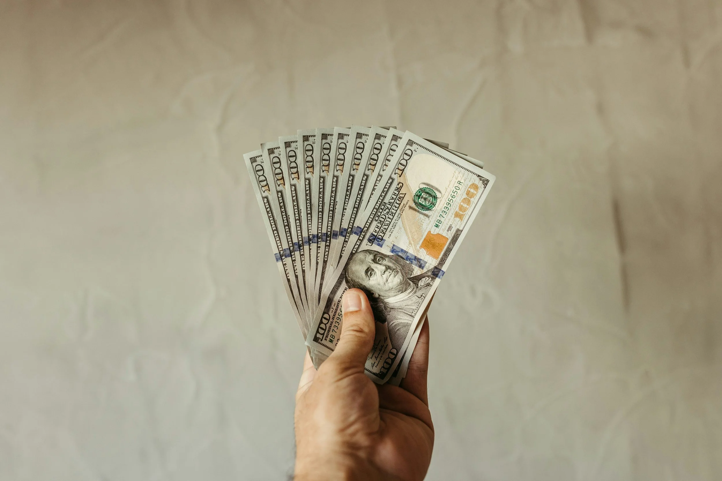 A hand holding many 100 dollar bils with a blank background