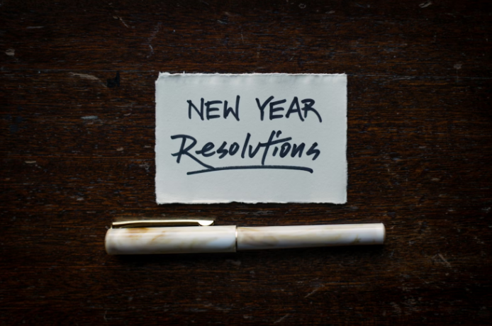 a white piece of paper that reads: "new year resolutions" on a dark background with a pen underneath