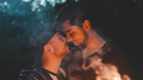Two men about to kiss holding a firework