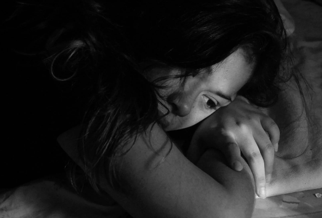 A girl laying her head down on her arms. The image is in black and white.