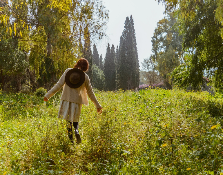 A woman wearing white walking through flowers and tall grass.