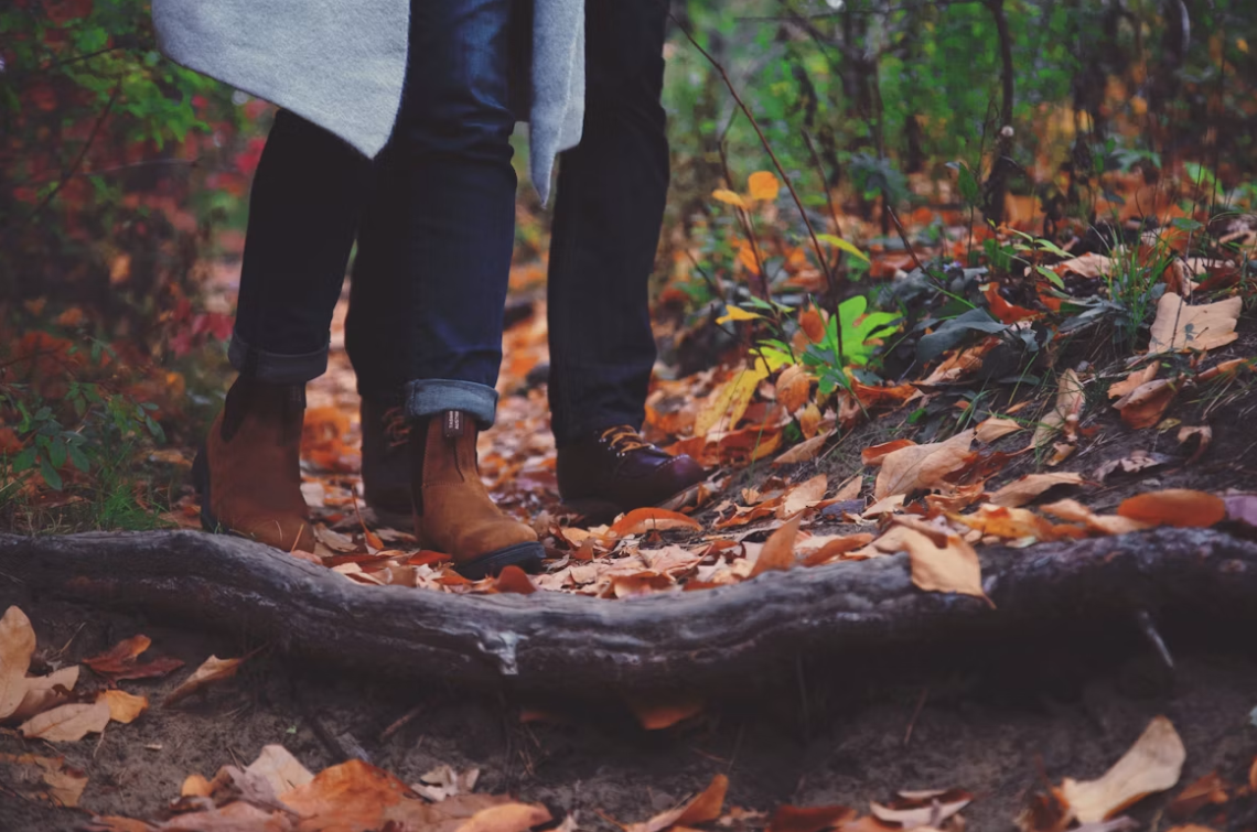 A close-up of a couple's shoes, walking together on a leaf-laden path