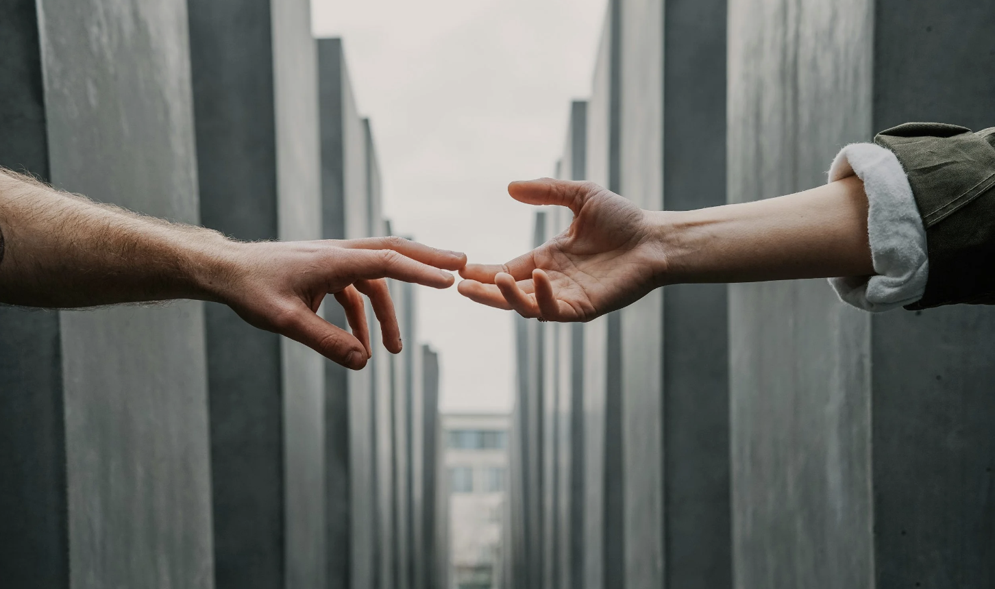 A photo of two hands reaching from opposite ends of the frame, meeting in the middle.