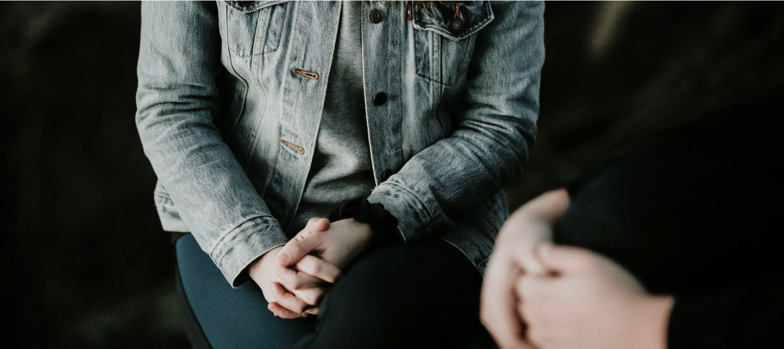 A photo of someone sitting down with their hands clasped in their lap.