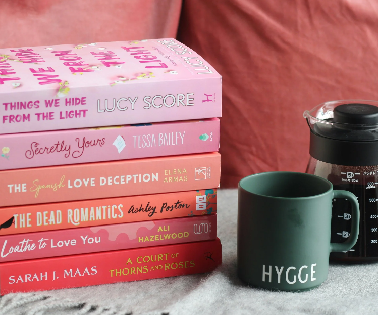 A stack of pink books are on the left. There is a green coffee mug next to a pot of coffee on the right.