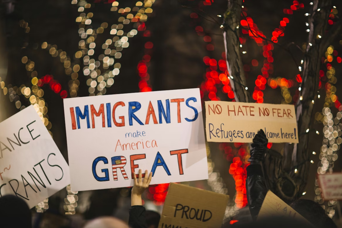 Protest signs with phrases like "Immigrants make America Great" and "No Hate No fear, Refugees are Welcome Here"