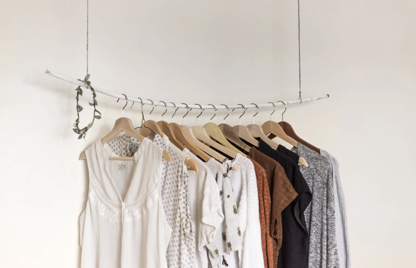 A hanging clothing rack with wooden hangers and light colored shirts