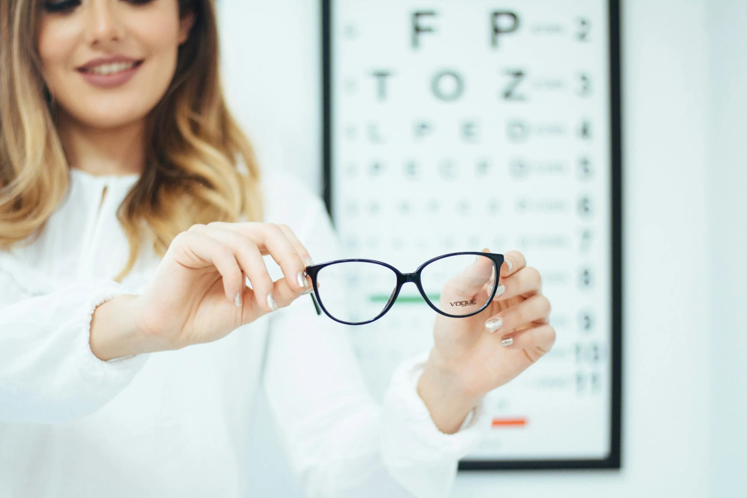 woman holding glasses standing in front of eye chart