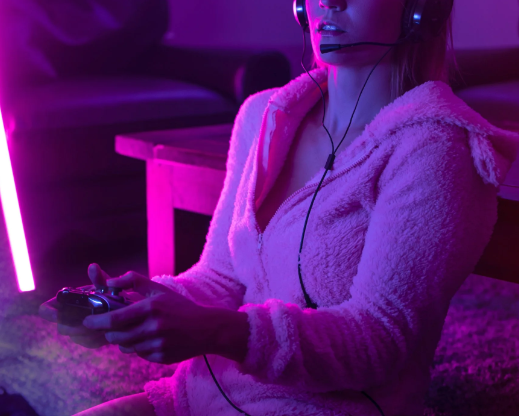 A woman wearing a headset and holding a gaming controller. The image has a pink and purple overlay.