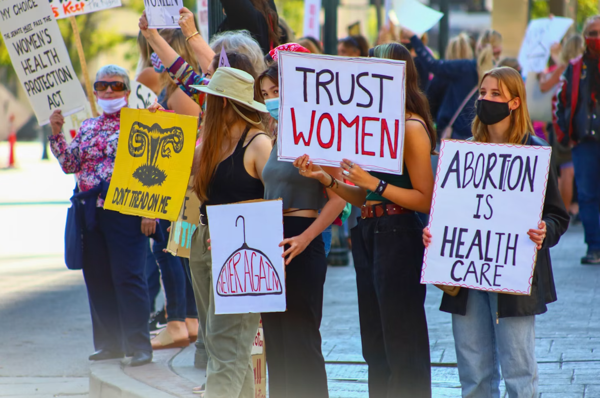 A group of women holding up pro-choice protest signs, some readinng "Trust Women" and "Abortion is Healthcare"