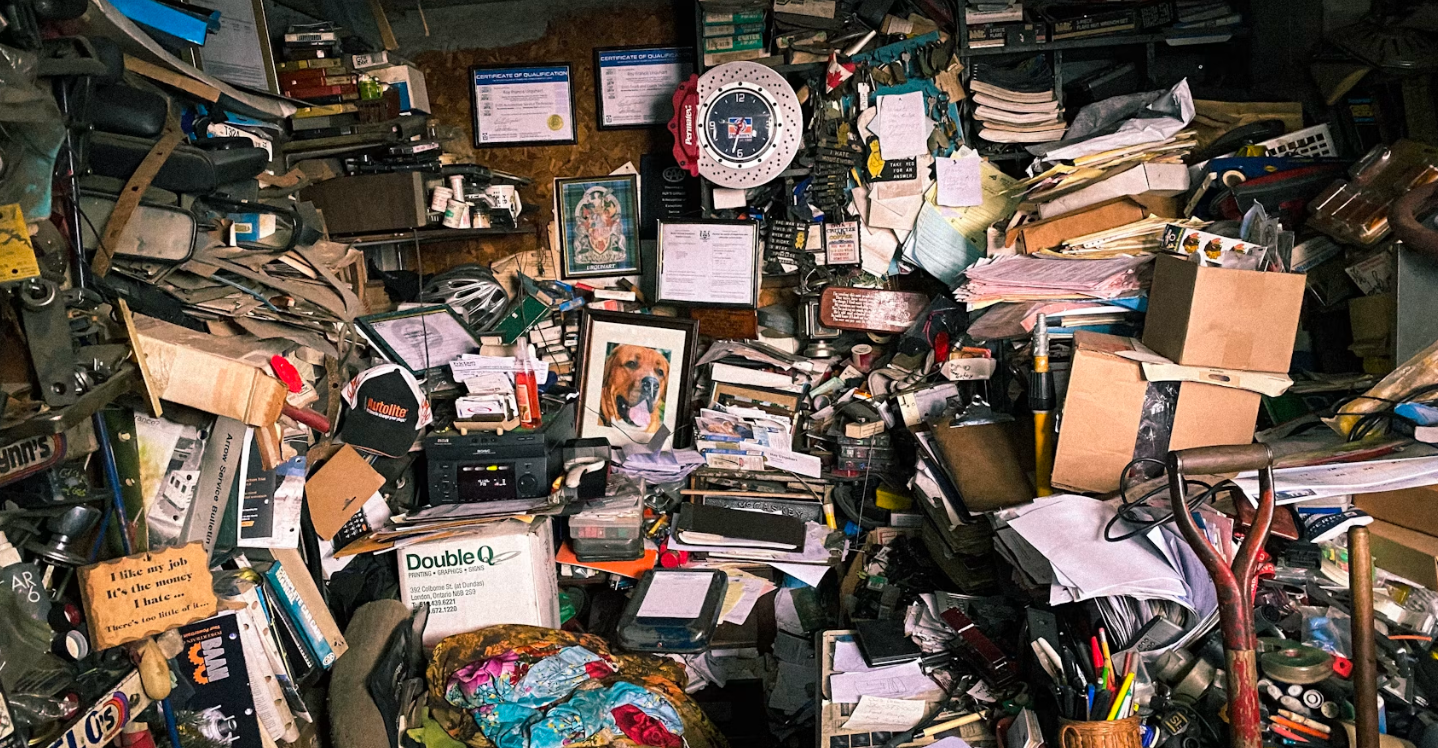 A cluttered garage, full of boxes, paintings, paper, and more.