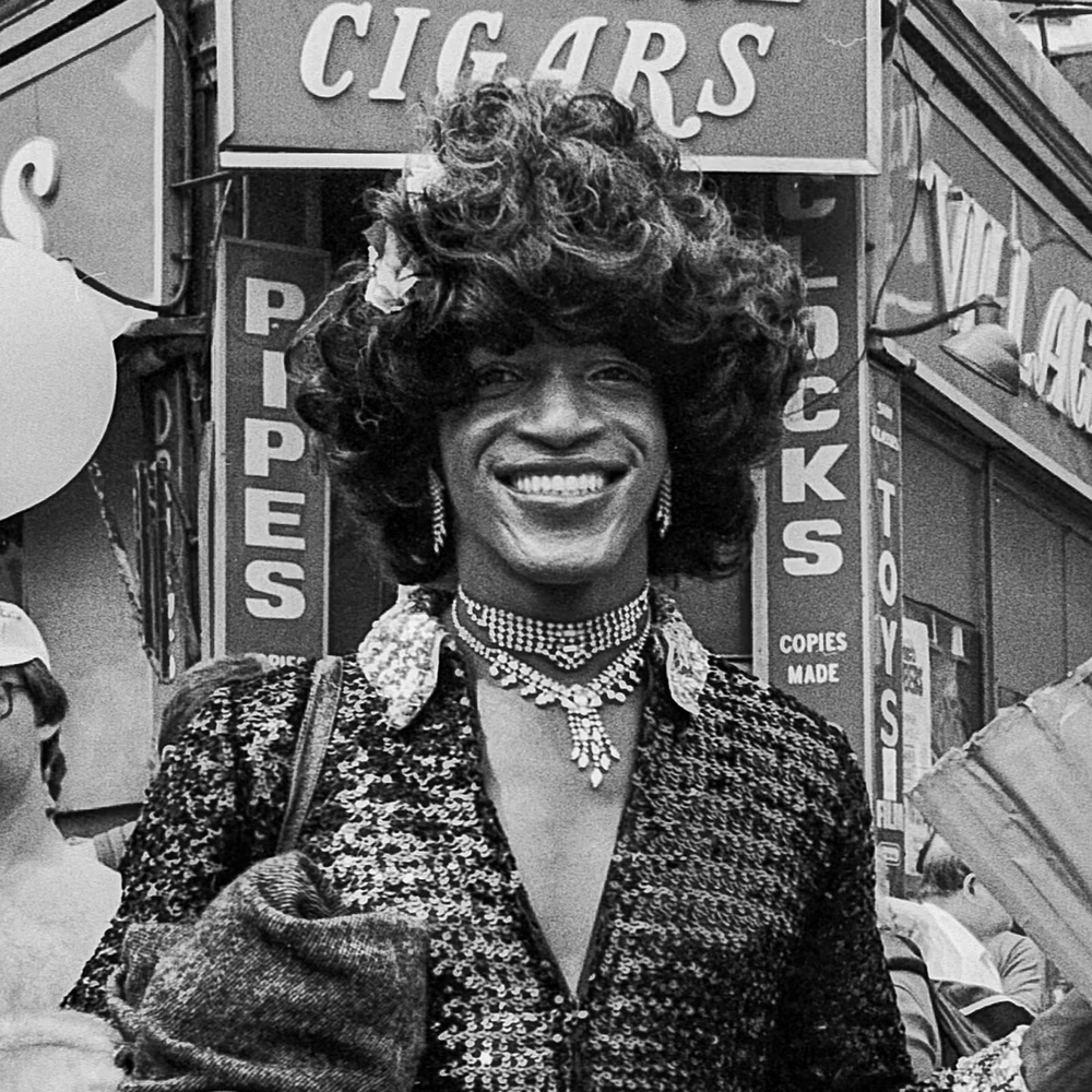 Marsha P Johnson smiling in front of a cigar store