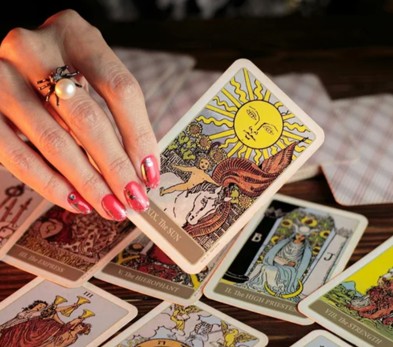 A manicured hand holding up "The Sun" tarot card