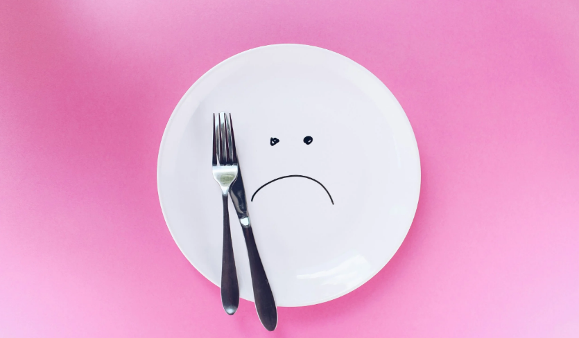 a white plate with a frowny face on it on a pink background with a knife and fork
