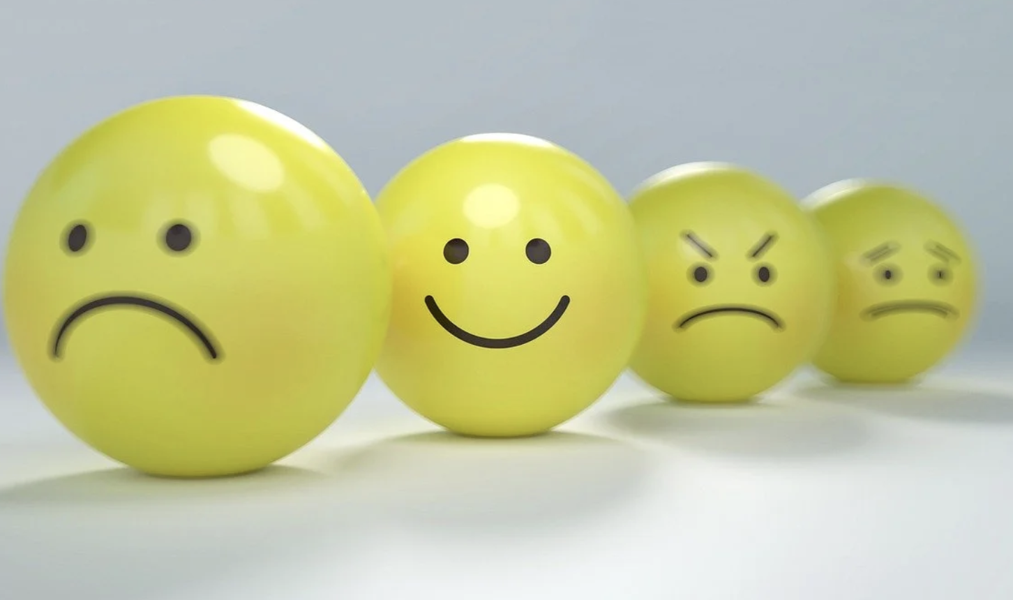 A photo of three yellow balls with different expressions on a white background. The center one is smiling.