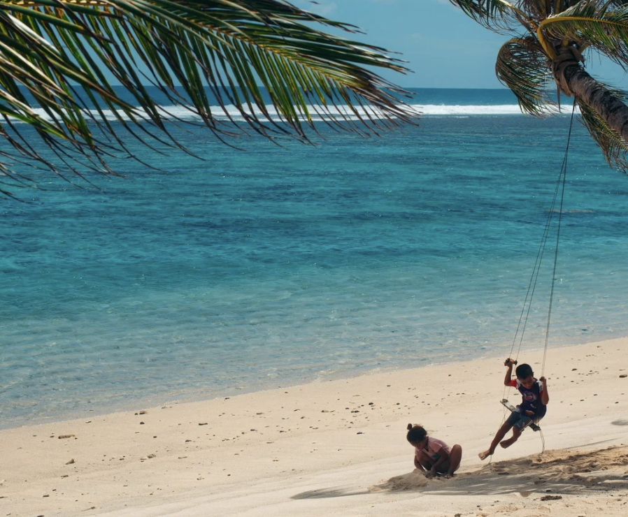 A photo of a person swinging on a beach next to someone else playing in the sand