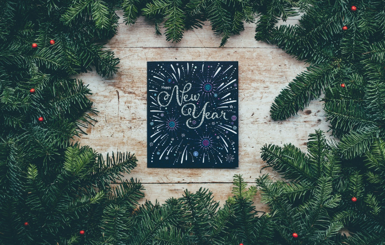 a blue square with "happy new year" calligraphied on it, with fireworks on the page and pine boughs surrounding the square