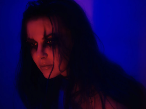 A photo of someone with red lighting and a blue background. Their hair is over their face and their face has a cut in it 