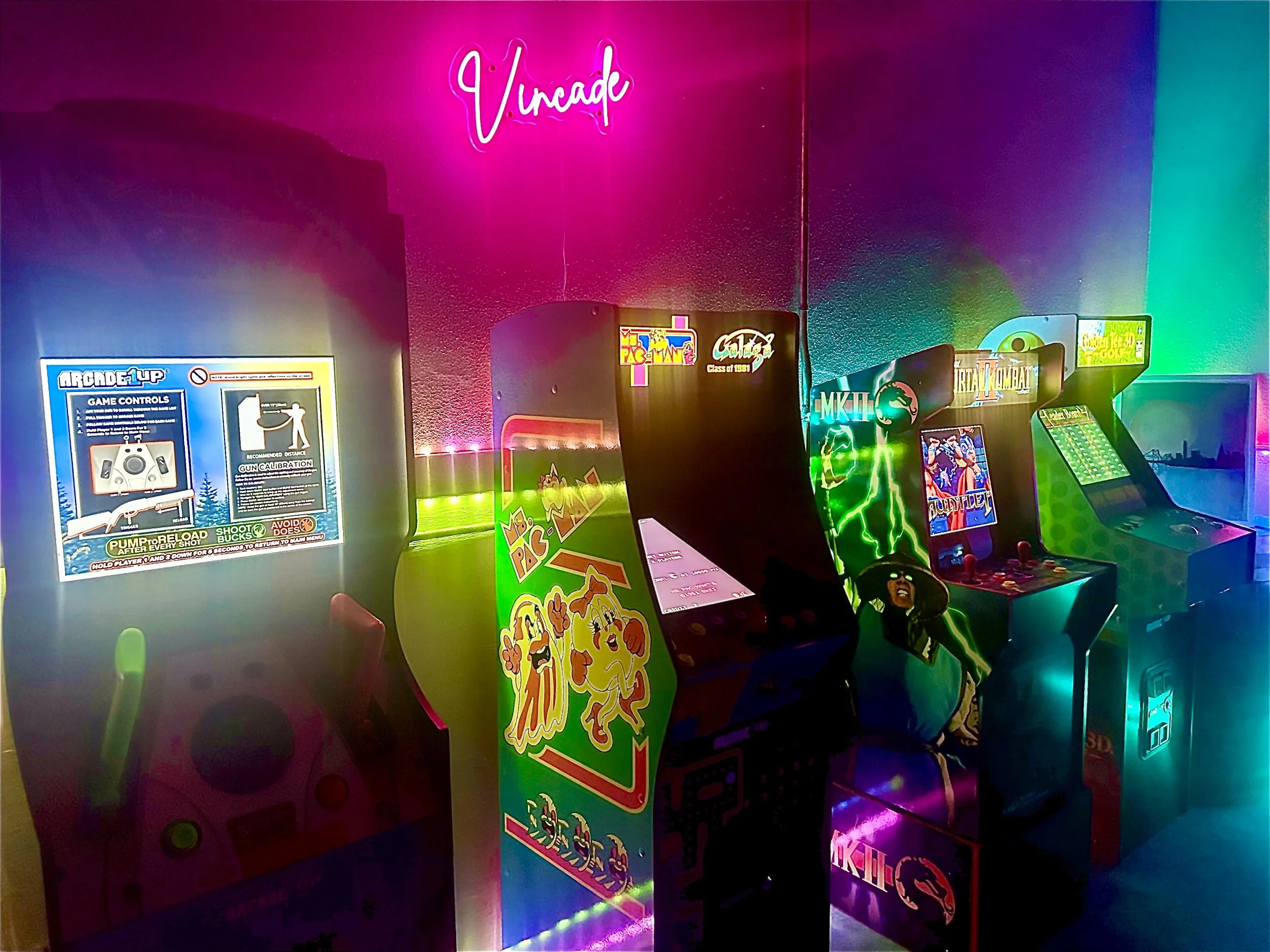 A row of vintage arcade game machines with colorful neon lighting in a gaming arcade. The machines feature games like Mortal Kombat and others, with a pink neon sign reading 'Uncade' on the wall.