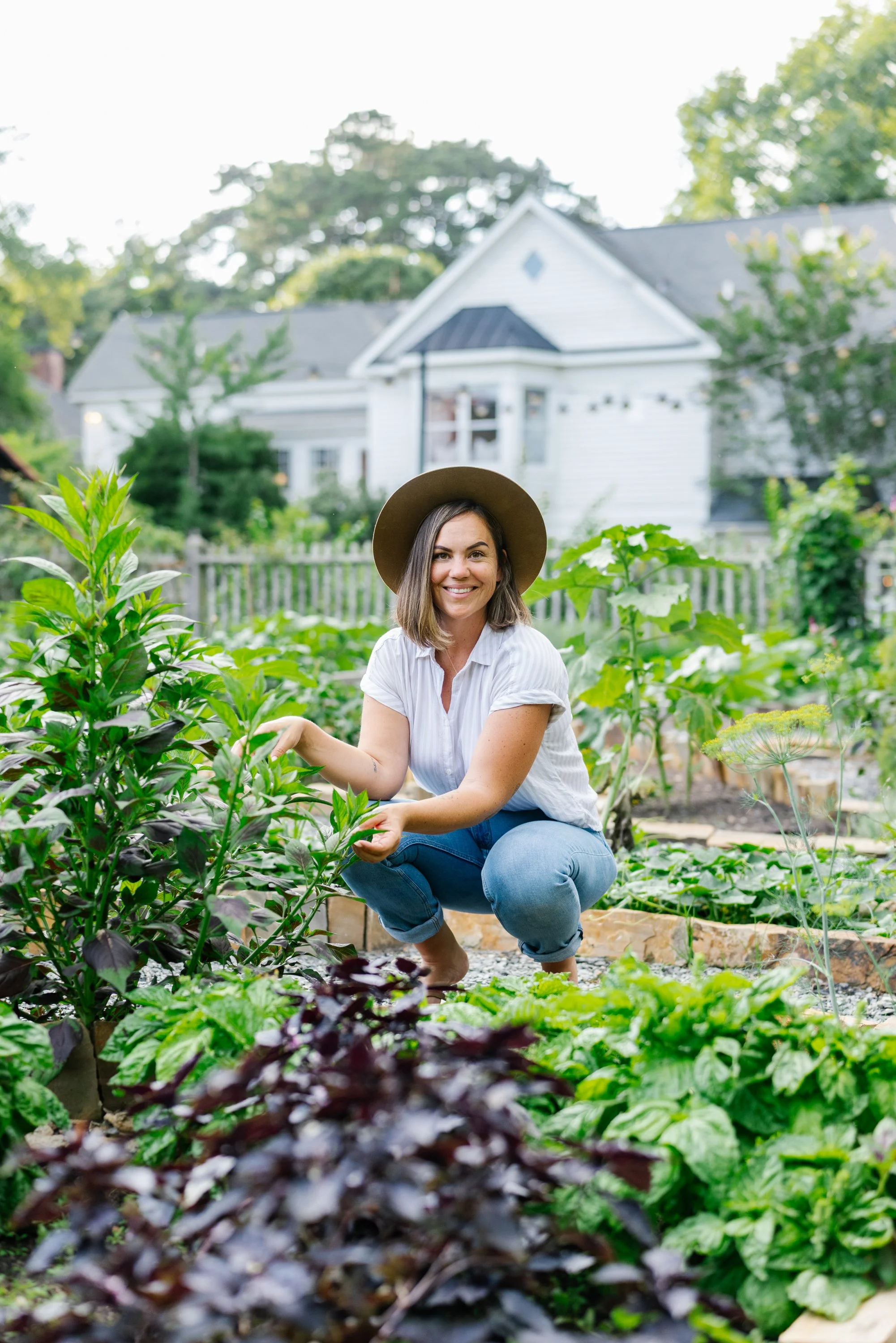 Woman in a hat tending plants in a backyard vegetable garden