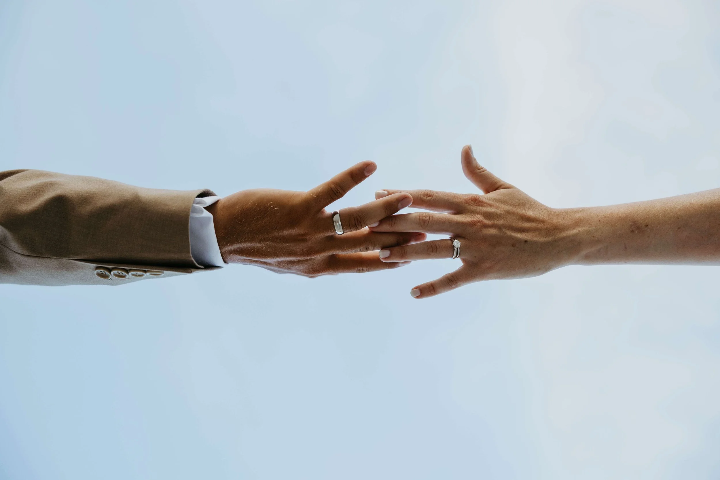 Couple on their wedding day reaching for each other showing off their wedding rings in downtown Sioux Falls shot by Jenna Heckel Photography.