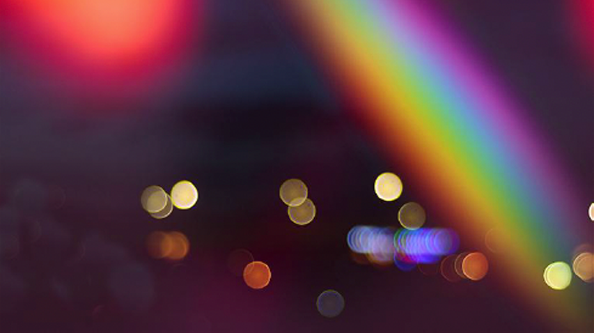 Blurred city lights with a rainbow rainbow light streak across the top right corner.