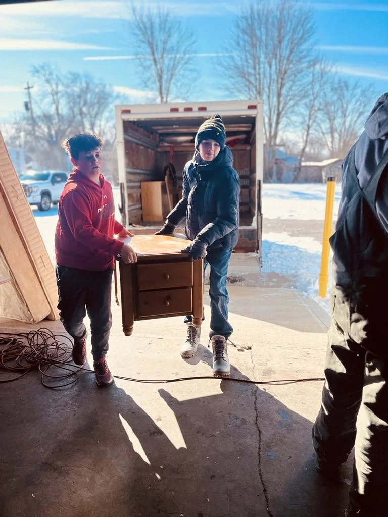 Two teens boys unloading an end table from the furniture truck to the furniture warehouse.