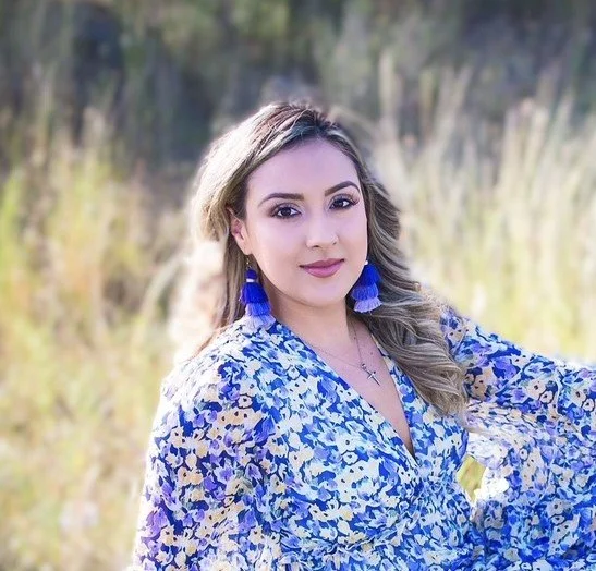 This is a picture of Patty in a floral dress sitting in a field. She is a maternal mental health counselor and perinatal therapist.