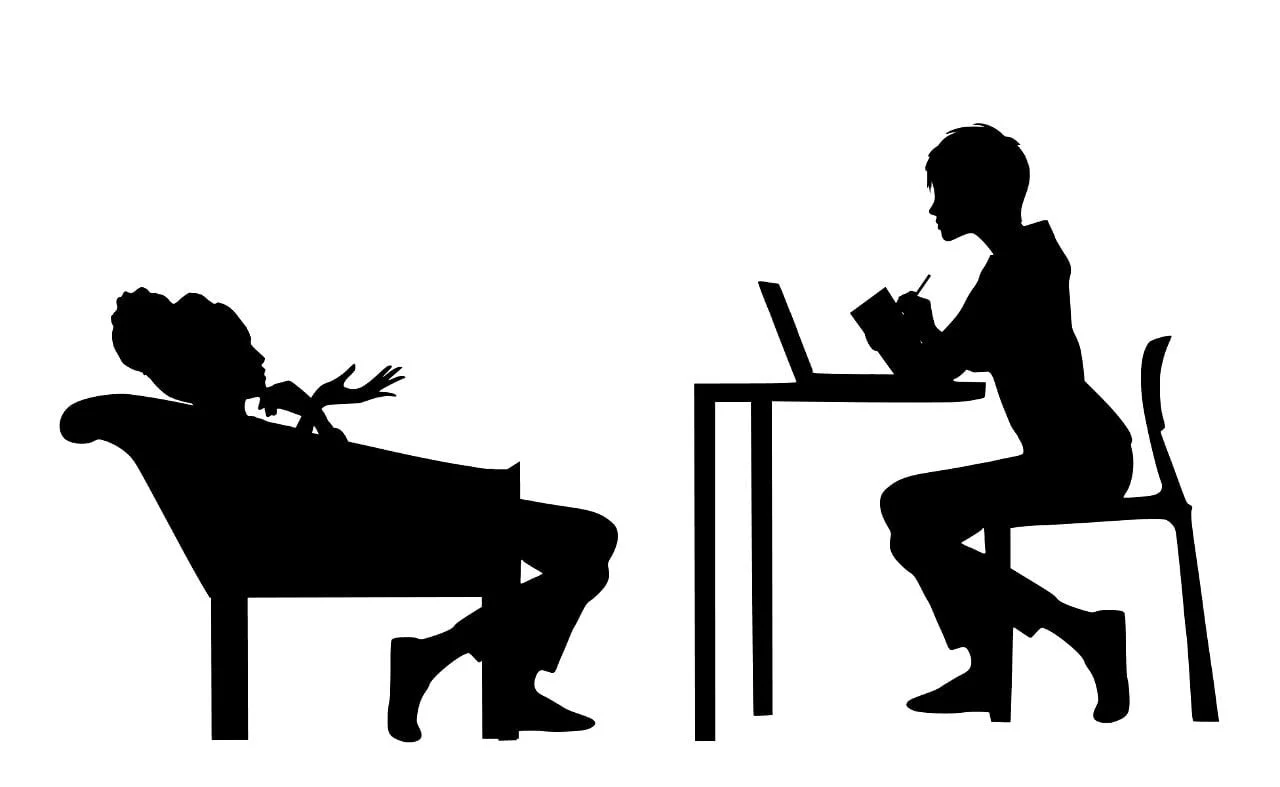 This is a photo of 2 women talking while one is attending therapy for adults in San Antonio and Schertz. One is sitting at a desk and the other woman is sitting in a chair