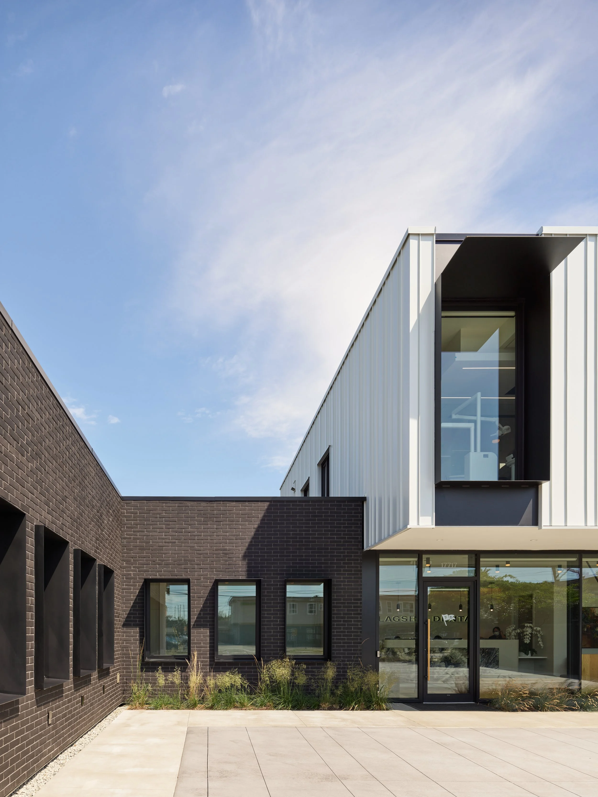 Contemporary commercial dental clinic facade with dark brick, light metal panels and large clear glass windows.