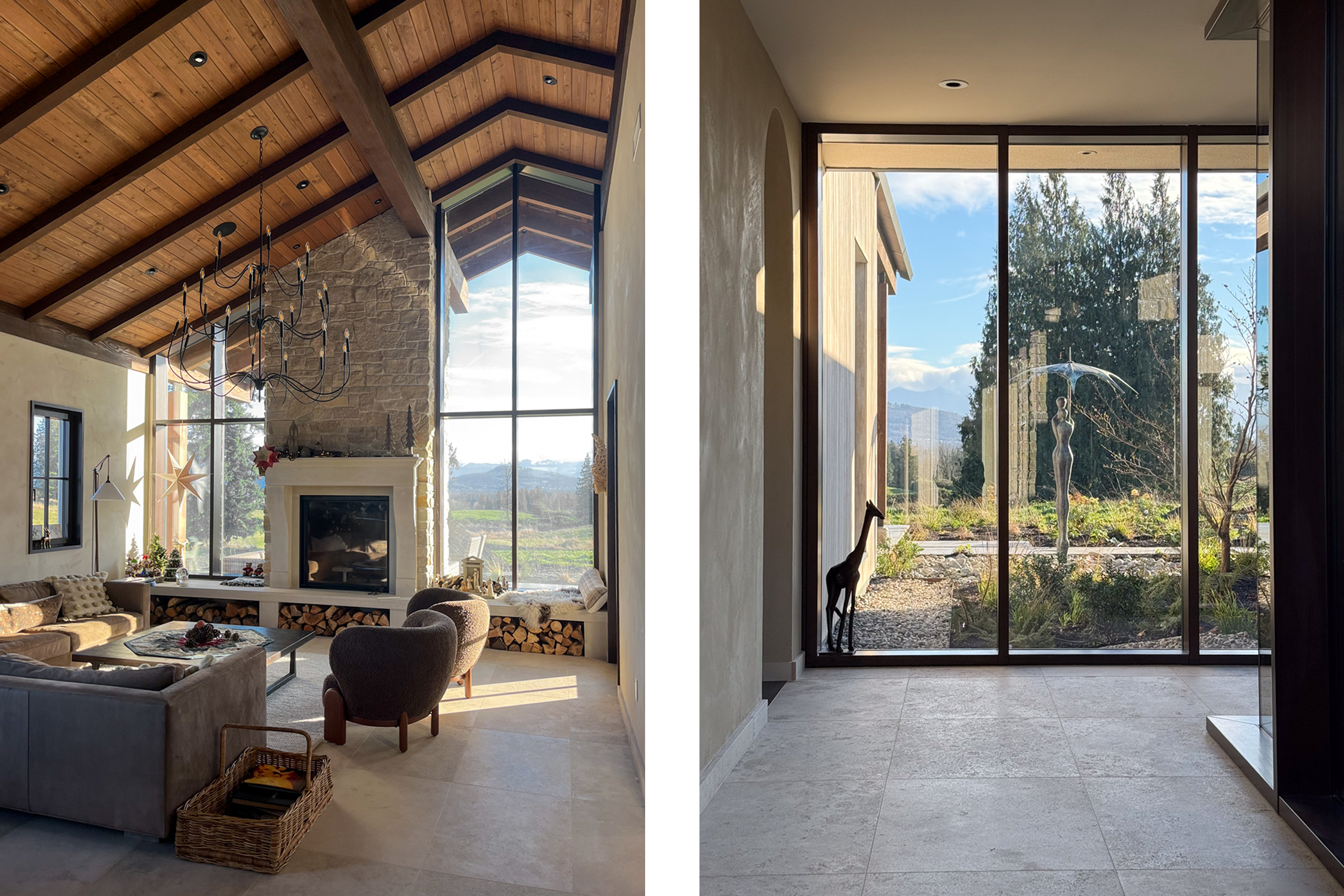 Interior view of a modern living room with high vaulted wooden ceiling, large windows overlooking the outdoors, a stone fireplace, and comfortable seating furniture. The outside scene shows mountains and trees.
