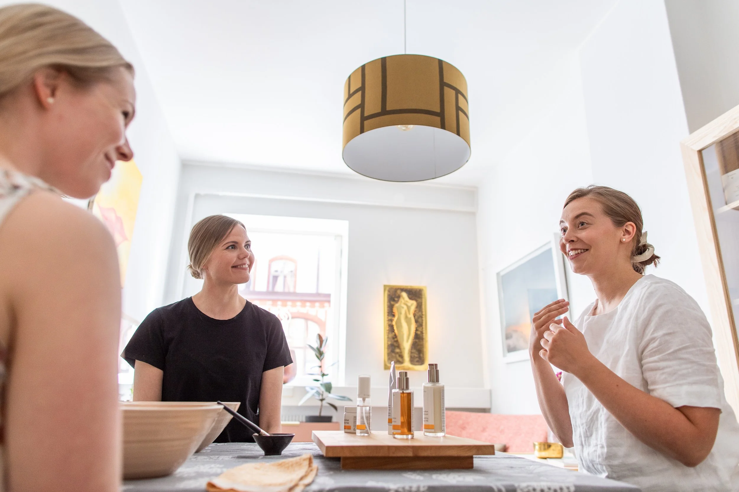 Kolme naista nauttii keskustelusta keittiössä, jolla on erilaisia kosmetiikkatuotteita.