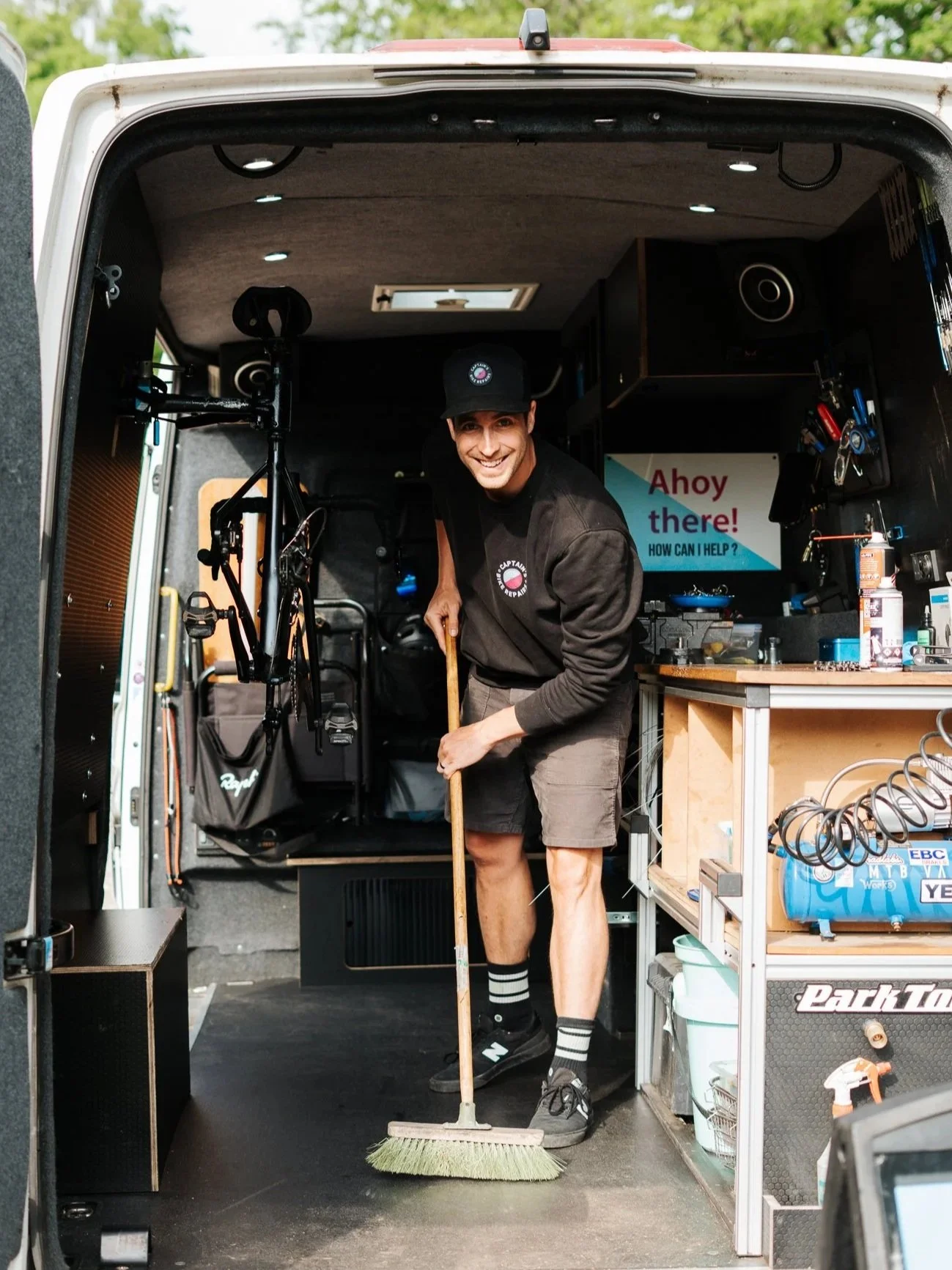 Chris, Captain's bike repairs mechanic and owner, sweeping the floor inside a mobile workshop or maintenance van.