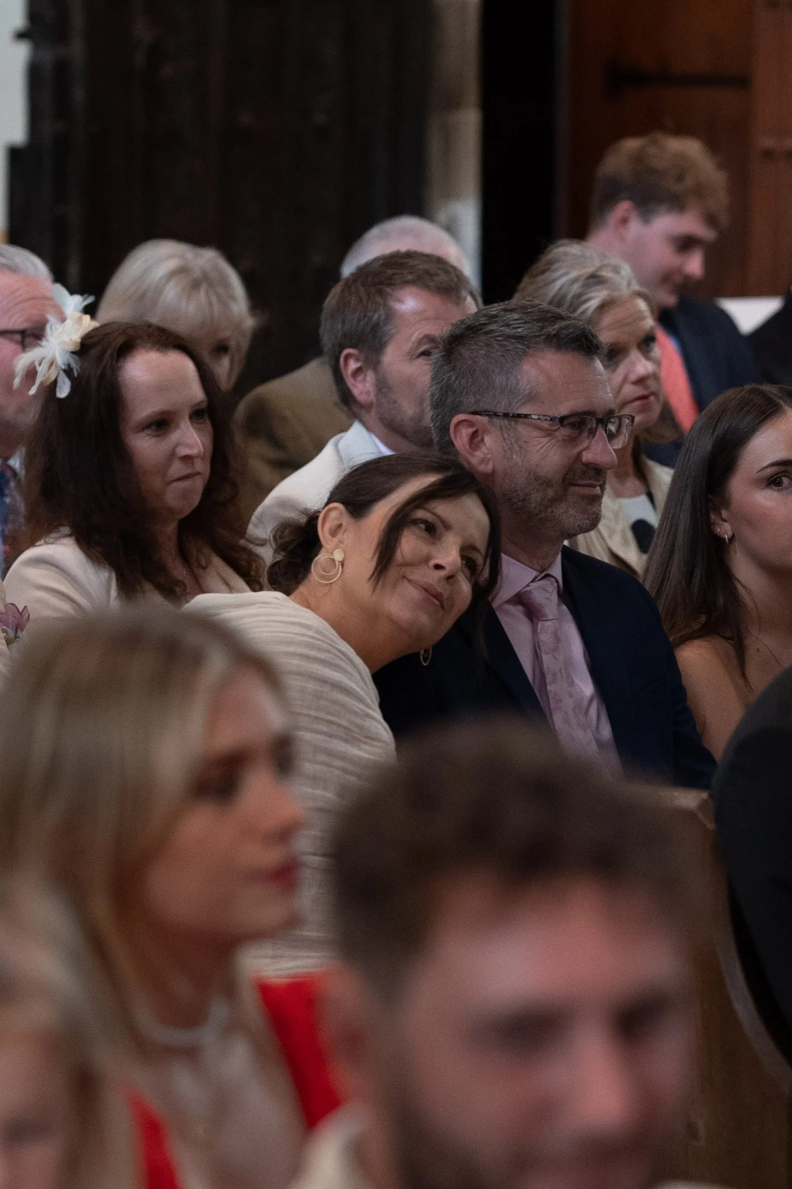 People seated in an audience, attending a formal event or ceremony, with some smiling and others focused on the occasion.